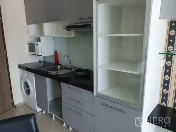 Condominium for rent in Khlong Toei, Bangkok - Compact modern kitchen with black countertops, sink, range hood, microwave, shelving, and in-unit washing machine.