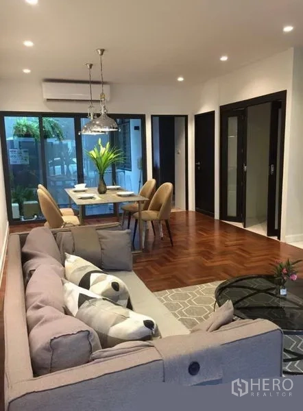 联排别墅 出租在Khlong Toei, Bangkok - 开放式客餐厅，转角沙发，拼花木地板，推拉玻璃门通向露台