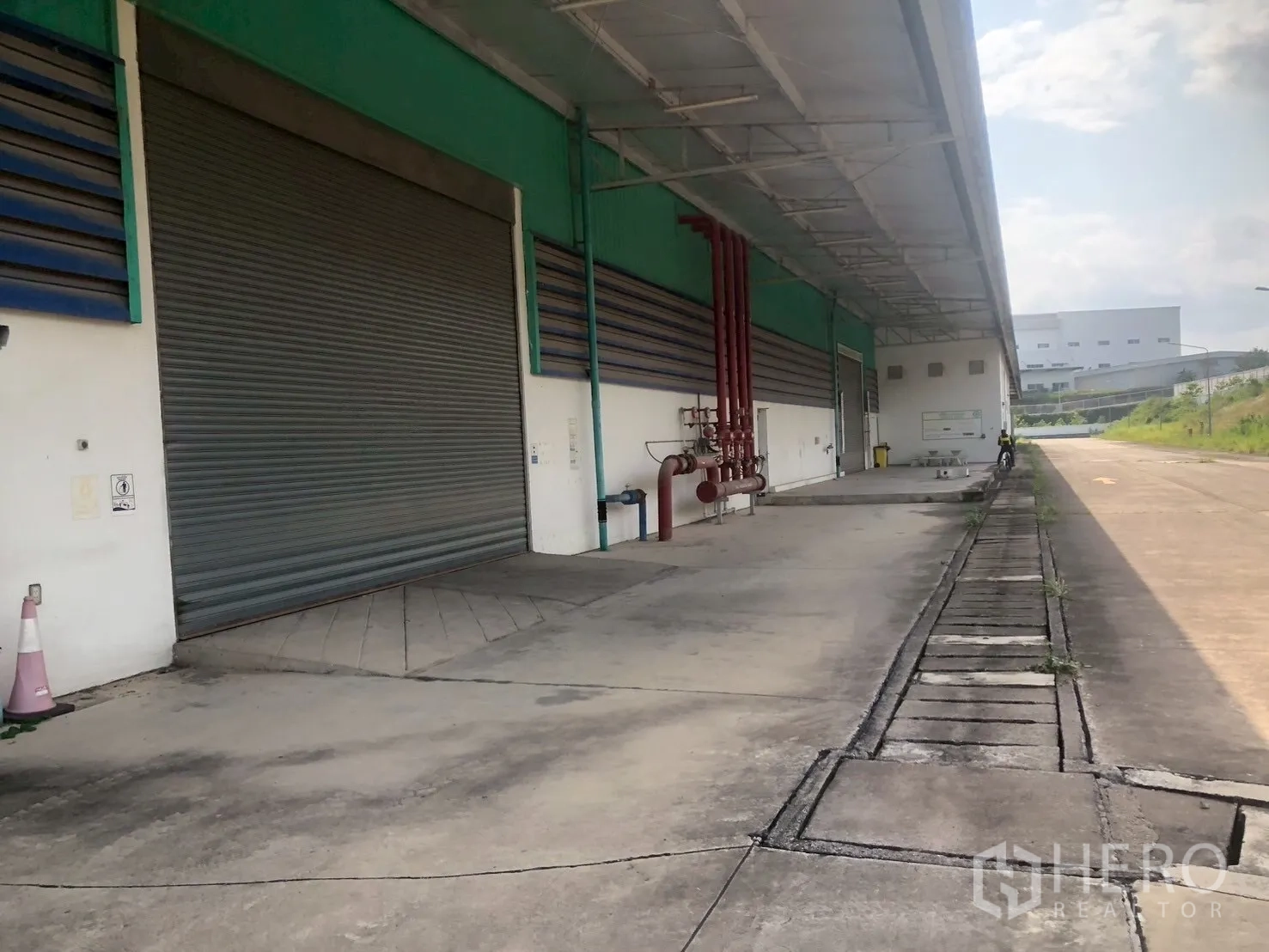 Factory for rent in Pluak Daeng, Rayong - Covered loading dock with large roller shutter doors and external fire piping along the wall.