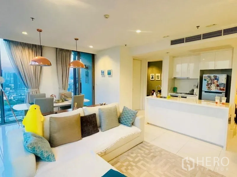 Condominium for rent or sale in Sathon, Bangkok - Living room with sectional sofa and adjacent open kitchen with island.