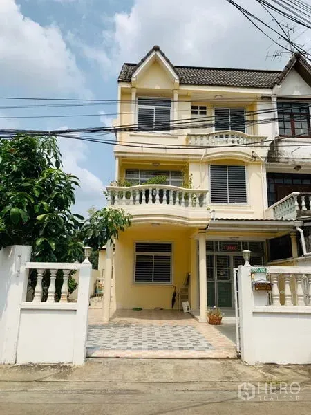 Townhouse for rent or sale in Huai Khwang, Bangkok - Three-storey yellow townhouse with gated parking and curved balconies in Huai Khwang, Bangkok