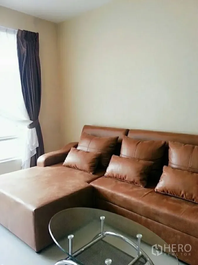 Condominium for rent in Khlong Toei, Bangkok - Cozy living room with brown leather sectional sofa and glass coffee table.
