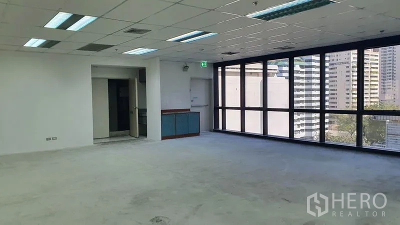 Office Space for rent in Watthana, Bangkok - Open workspace with large windows, a small pantry alcove, and doorway access.