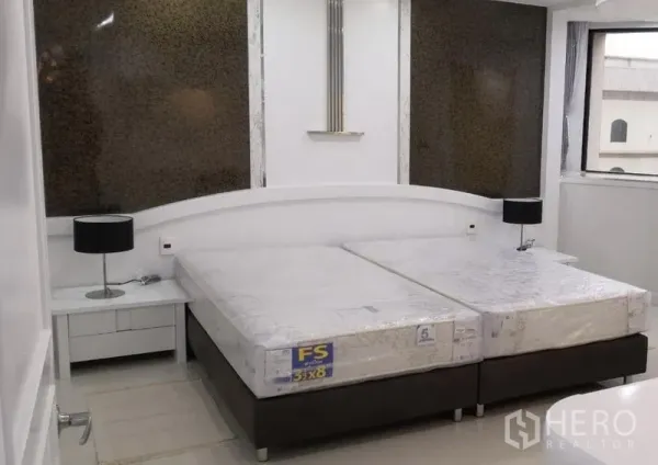 Condominium for rent in Khlong Toei, Bangkok - Bedroom with twin mattresses on a platform bed, bedside tables with black lamps and large windows.