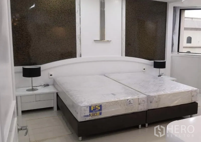 Condominium for rent in Khlong Toei, Bangkok - Bedroom with twin mattresses on a platform bed, bedside tables with black lamps and large windows.