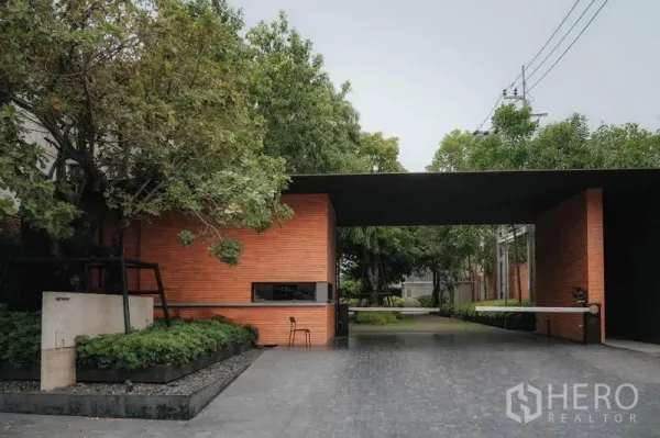 Townhouse for rent - Gated entrance with brick guardhouse and tree-lined driveway at an upscale townhouse community in Saphan Sung