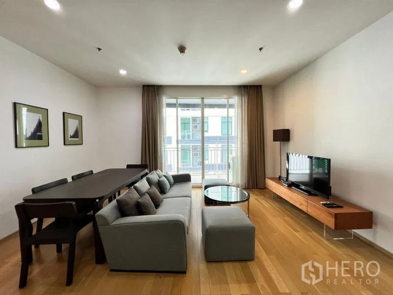 公寓 出租在Khlong Toei, Bangkok - 开放式客餐厅，灰色沙发与长餐桌，落地门通往阳台。