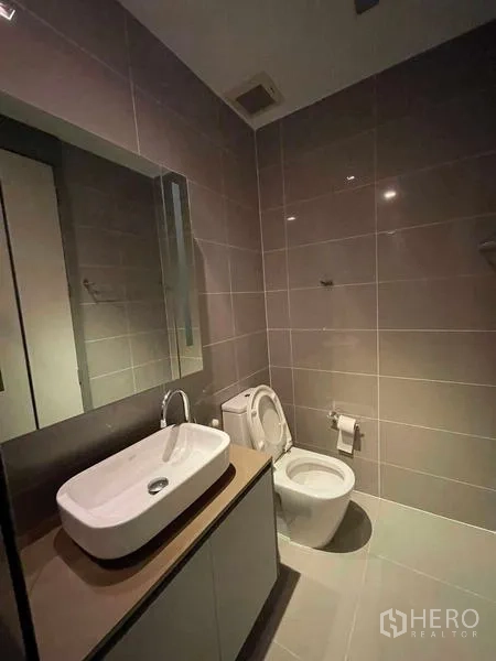 Condominium for rent or sale in Bang Rak, Bangkok - Second bathroom with glossy gray tiles, vessel sink, mirror, and toilet.
