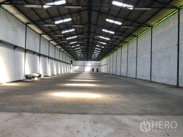 Factory for rent in Nonthaburi - Large clear-span factory hall with high gable roof, steel trusses, skylights and concrete floor.