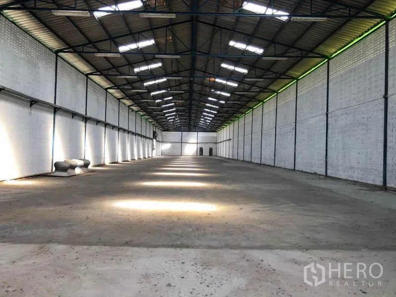 Factory for rent in Nonthaburi - Large clear-span factory hall with high gable roof, steel trusses, skylights and concrete floor.