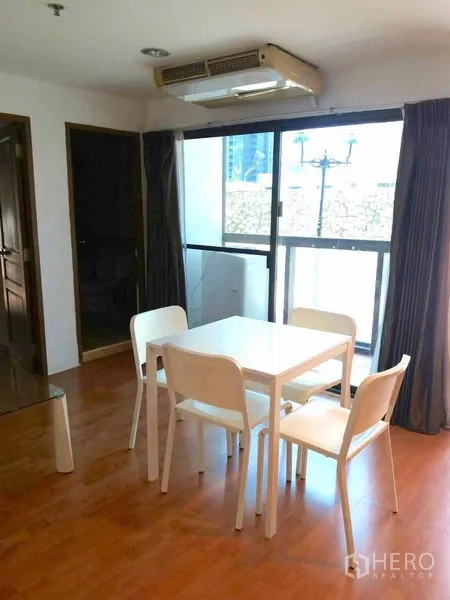Condominium for rent in Watthana, Bangkok - Dining area with four‑seat white table next to sliding glass door leading to a small balcony.