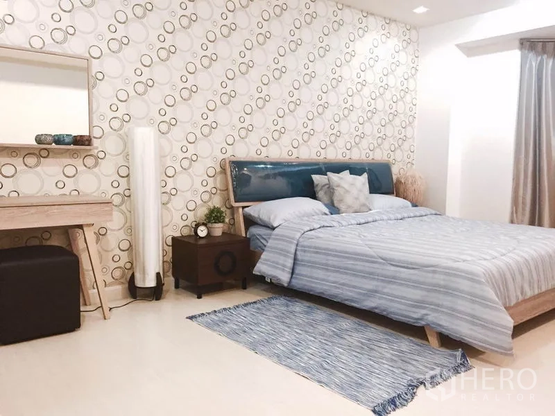 Condominium for rent or sale in Watthana, Bangkok - Master bedroom with patterned wallpaper, blue bedding, dressing table and soft natural light.