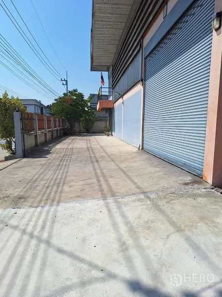 货栈 出售在Pathum Thani - 仓库前方宽阔混凝土装卸区，设多扇蓝色卷帘门。