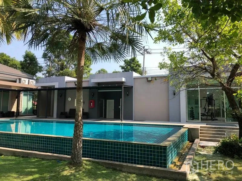 独立式住宅 出售在Nonthaburi - 社区室外泳池，旁边是会所与树荫。