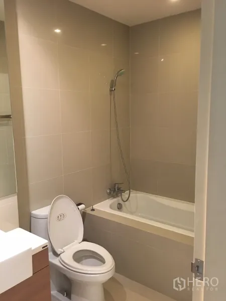 Condominium for rent in Phaya Thai, Bangkok - Contemporary bathroom with bathtub, handheld shower, toilet and vanity in beige tiles.