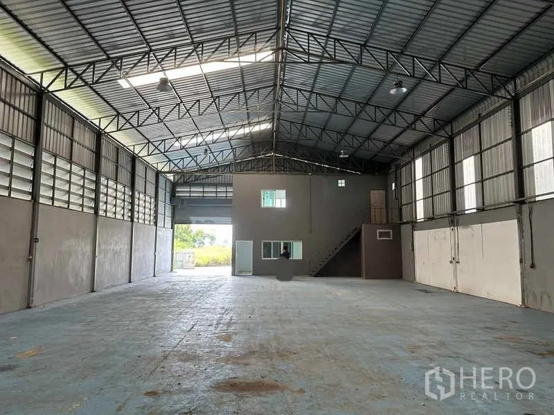 Warehouse for rent in Pathum Thani - Spacious warehouse interior with high steel truss roof, skylights and a small mezzanine office with stair.