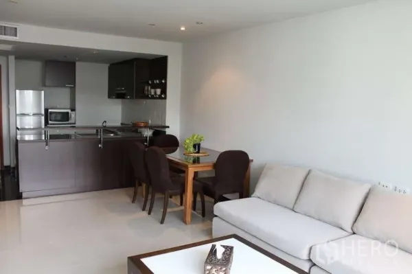 Condominium for rent in Sathon, Bangkok - Open-plan living and dining area with a light sofa, four-seat table, and a dark wood kitchen in a modern condo.