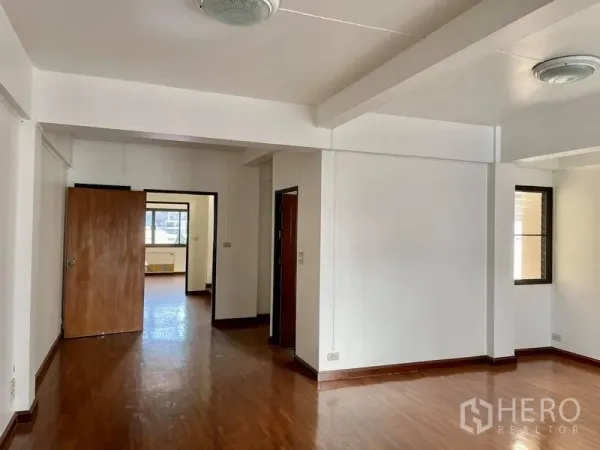 Home Office for rent in Khlong Toei, Bangkok - Spacious unfurnished room with white walls, wood floors and multiple doorways in a home office.