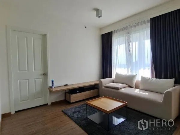 Condominium for rent or sale in Yan Nawa, Bangkok - Bright living room with sofa, coffee table, TV console and large curtained windows.