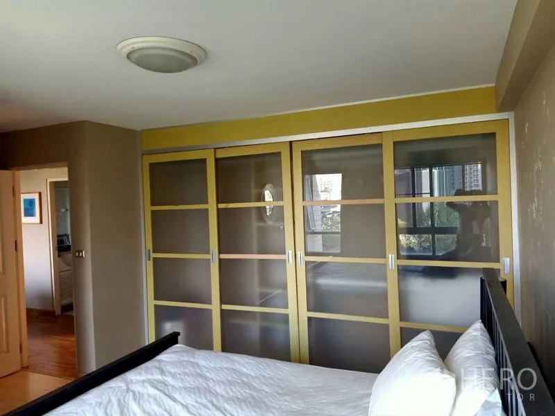 Condominium for rent in Khlong Toei, Bangkok - Master bedroom with large frosted sliding wardrobes and a city-view window.