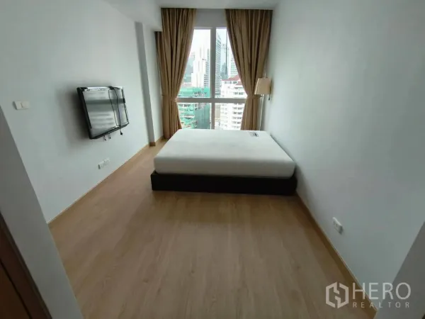 Condominium for rent in Khlong Toei, Bangkok - Master bedroom with city-view window, double bed, wall-mounted TV, and beige curtains.