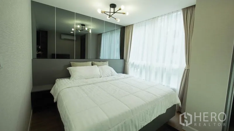 Condominium for rent in Khlong San, Bangkok - Cozy guest bedroom with mirrored headboard, large window, and contemporary light fixture.