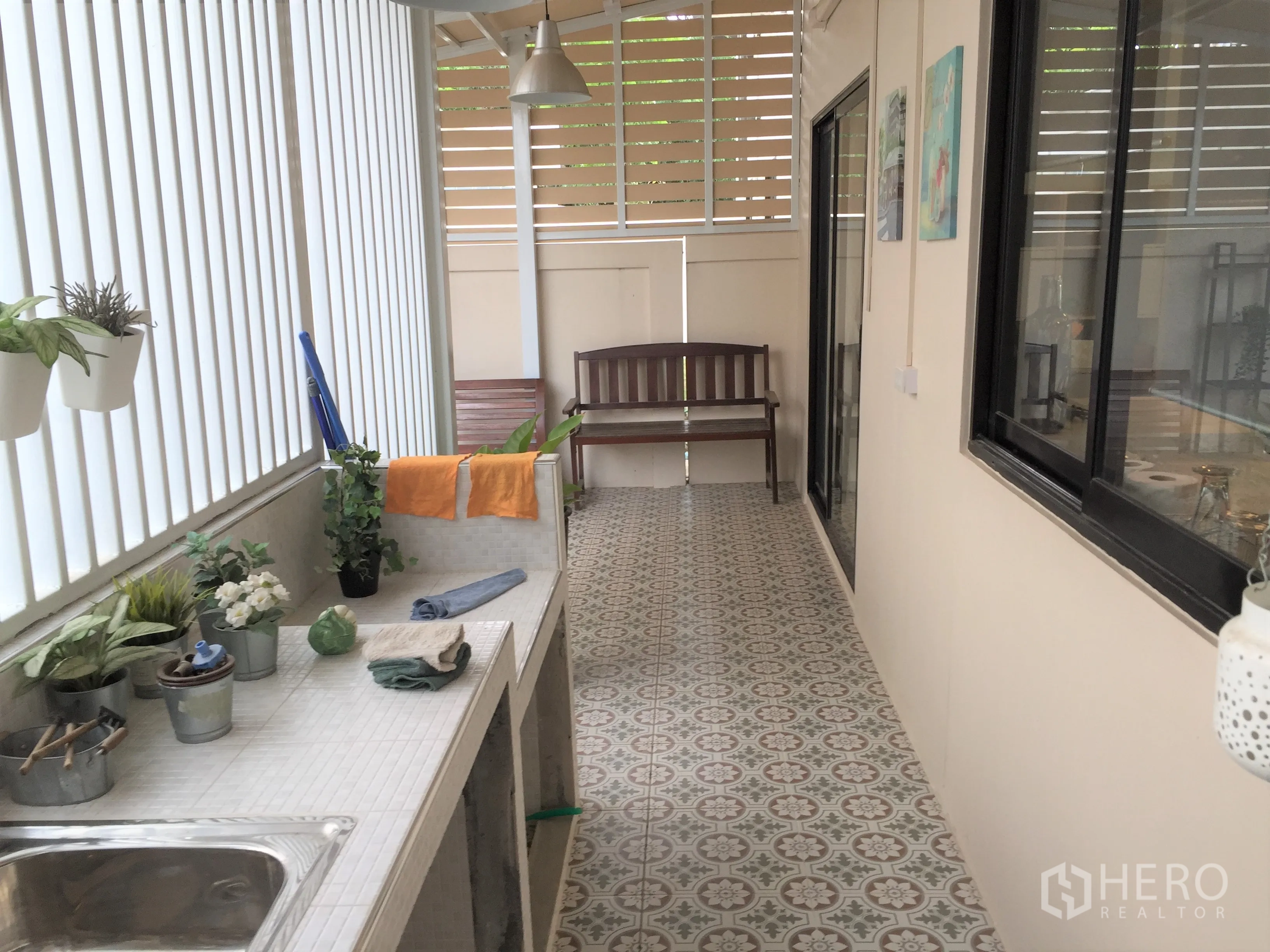 Townhouse for rent in Saphan Sung, Bangkok - Covered side patio with patterned tiles, utility counter and sink, potted plants and bench.