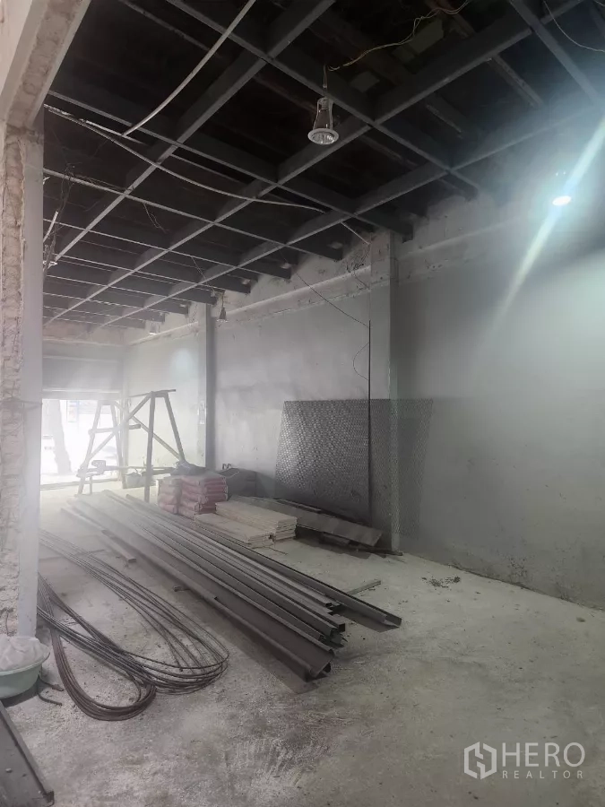Shophouse for rent in Watthana, Bangkok - Open-plan workshop area with steel sections, ceiling grid and cement bags.