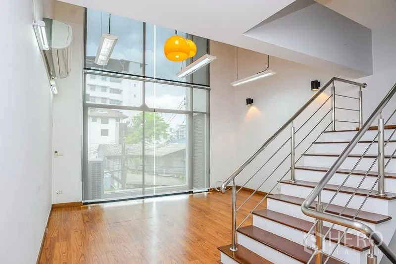 Townhouse for rent in Watthana, Bangkok - Double-height living area with floor-to-ceiling window and staircase overlooking the street view.