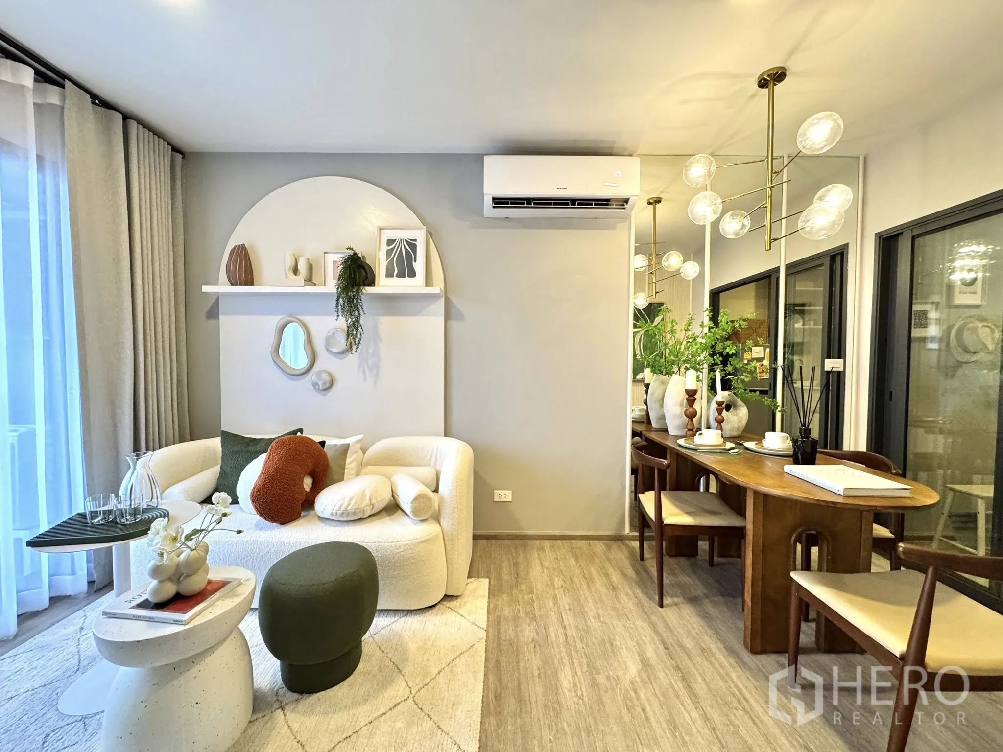Condominium for rent in Watthana, Bangkok - Living area with white sofa, wooden dining table, mirror wall, and pendant chandelier.