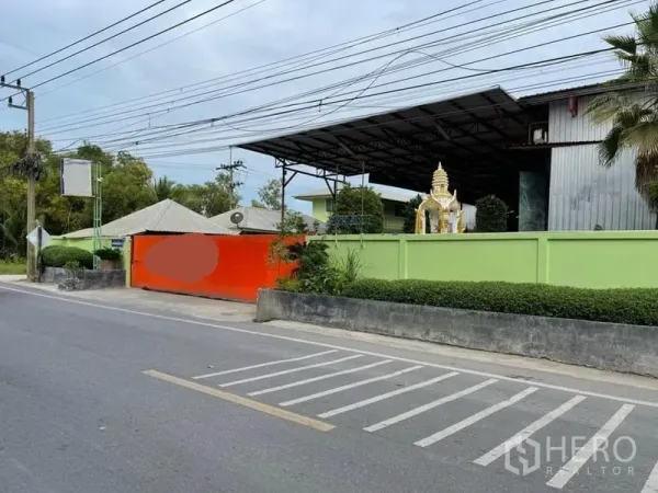 คลังสินค้า ขายในLam Luk Ka, Pathum Thani - ทางเข้าโกดังติดถนน มีกำแพงสีเขียว ประตูส้ม และอาคารหลังคาเหล็กภายใน
