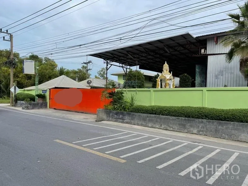 คลังสินค้า ขายในLam Luk Ka, Pathum Thani - ทางเข้าโกดังติดถนน มีกำแพงสีเขียว ประตูส้ม และอาคารหลังคาเหล็กภายใน