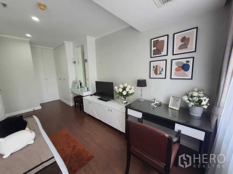 房间 出租在Watthana, Bangkok - 卧室工作角，书桌、电视柜、墙面装饰与花卉摆设。