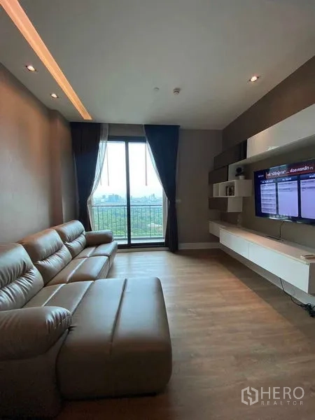 Condominium for rent in Bangkok - Cozy living room with leather sofa, TV wall and sliding door to a balcony facing park and city views.