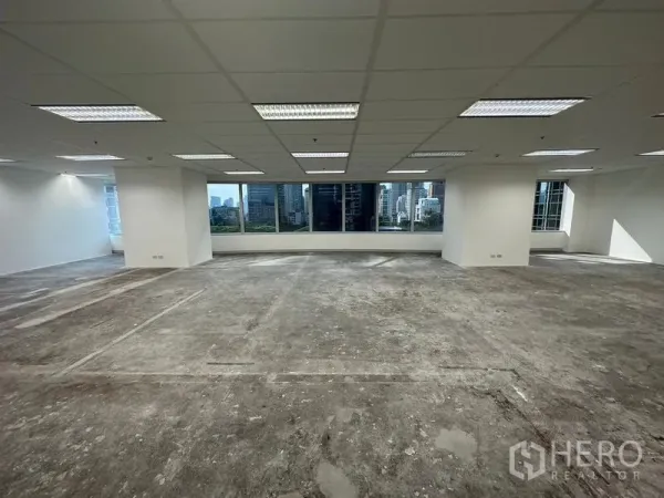 Office Space for rent - Open-plan office with suspended ceiling lights, large windows and Bangkok skyline views, unfinished concrete floor ready for fit-out.