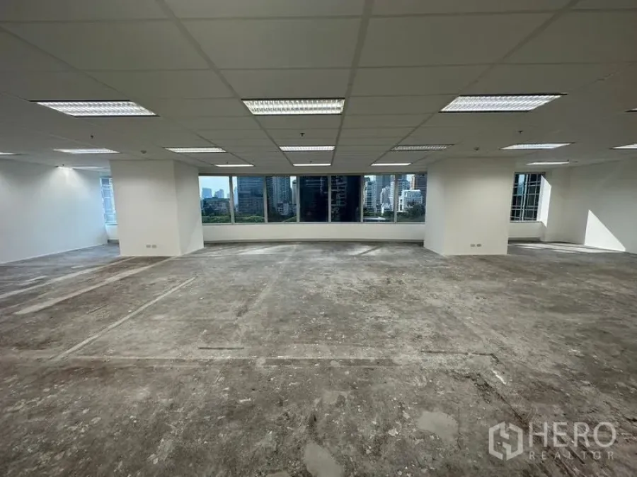 Office Space for rent - Open-plan office with suspended ceiling lights, large windows and Bangkok skyline views, unfinished concrete floor ready for fit-out.