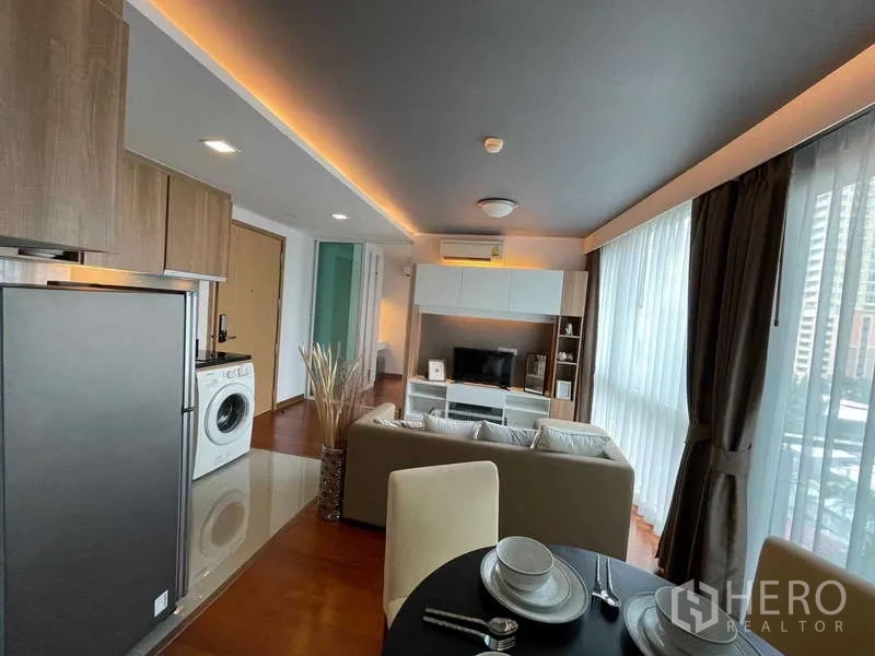 Condominium for sale in Watthana, Bangkok - Open-plan living and dining with floor-to-ceiling windows, fitted kitchen with fridge and washer, and TV console.