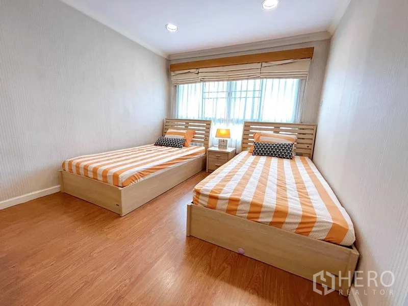公寓 出租在Watthana, Bangkok - 明亮卧室，双单人床，条纹床品，大窗与床头灯。
