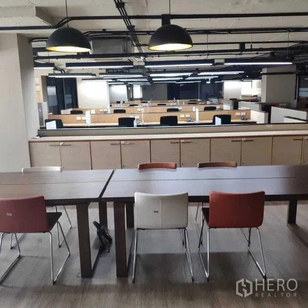 Office Space for rent - Open-plan office with rows of workstations and pendant lights, with a breakout table in front.