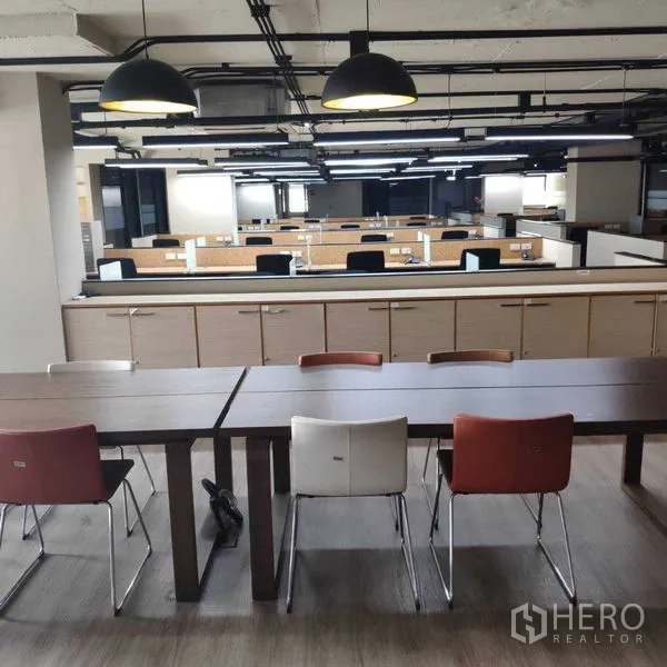 Office Space for rent - Open-plan office with rows of workstations and pendant lights, with a breakout table in front.