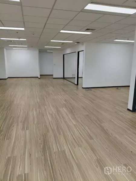 Office Space for rent - Long open office area with wood-look flooring and glass-partitioned rooms along the side.