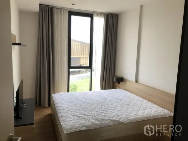 Condominium for rent in Watthana, Bangkok - Primary bedroom with large window, bed, and view of greenery and nearby buildings.