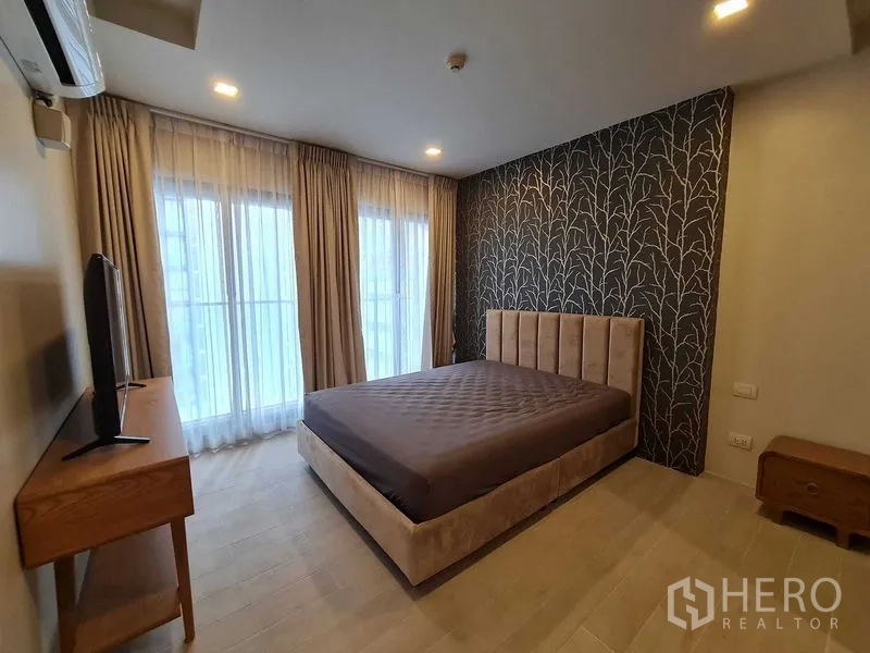 公寓 出租在Pathum Wan, Bangkok - 主卧配软包床、特色墙纸、电视柜与落地纱帘，采光良好。