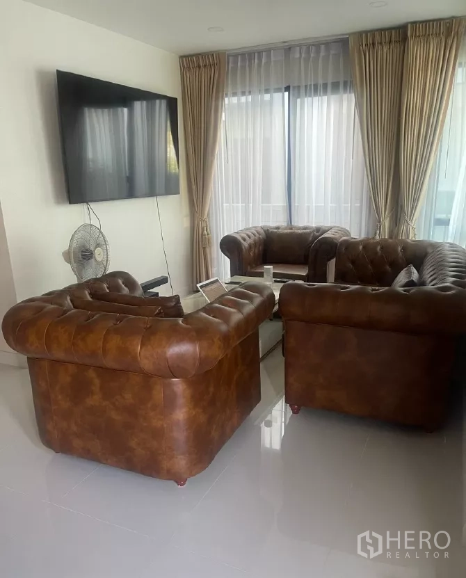 Detached House for rent or sale in Saphan Sung, Bangkok - Living room with wall-mounted TV and Chesterfield sofas facing glass doors.