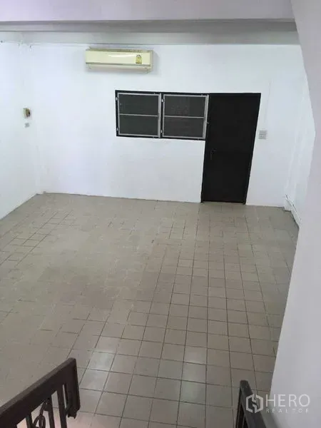 联排别墅 出租在Phra Khanong, Bangkok - 宽敞的瓷砖客厅，墙挂空调与黑色门窗。