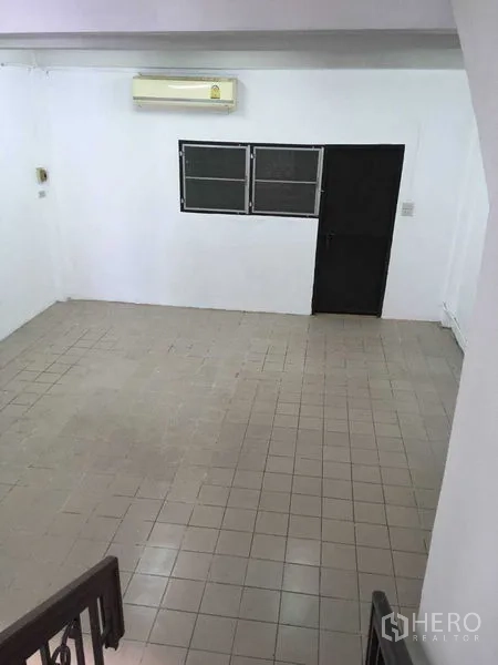 联排别墅 出租在Phra Khanong, Bangkok - 宽敞的瓷砖客厅，墙挂空调与黑色门窗。