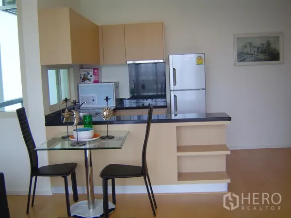 Condominium for rent in Chatuchak, Bangkok - Open kitchen with light wood cabinets, black granite breakfast bar, glass dining table and stainless refrigerator.