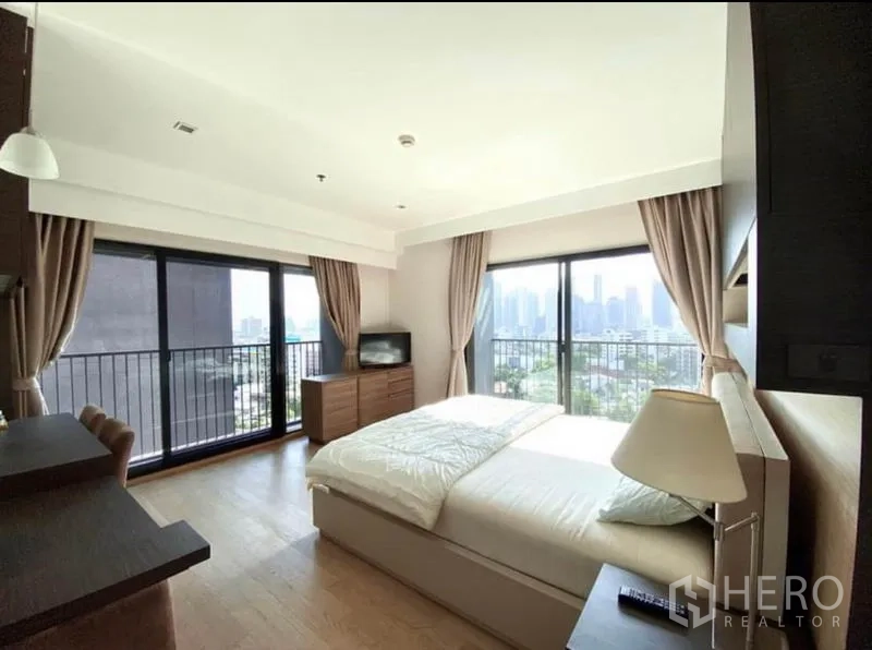 Condominium for rent in Khlong Toei, Bangkok - Corner bedroom with city views from two balcony doors and a queen bed.