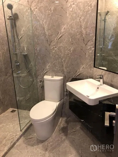 Condominium for rent in Watthana, Bangkok - Modern bathroom with marble-style tiles, glass-enclosed shower, square basin and toilet.