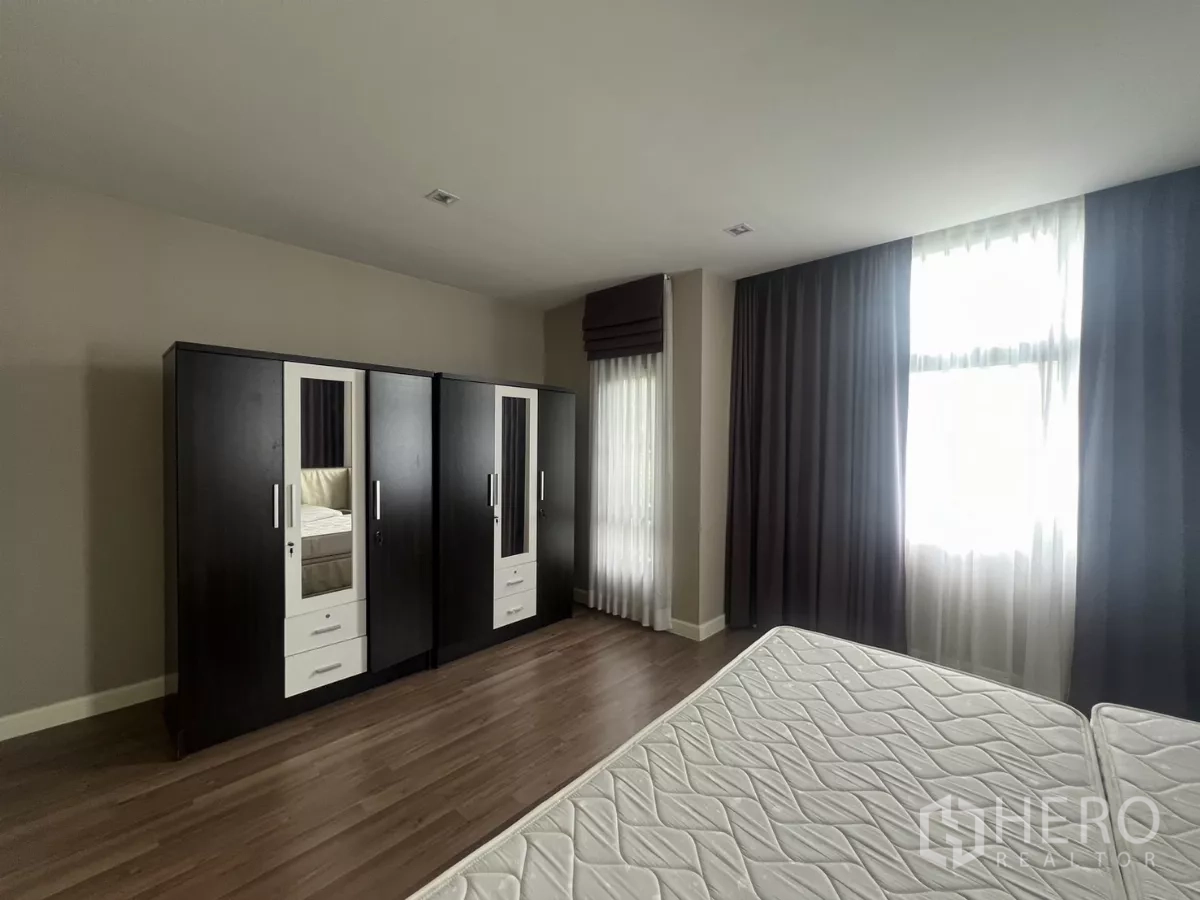 Detached House for sale in Bang Kapi, Bangkok - Bedroom wall with double wardrobes opposite the bed and wood flooring.